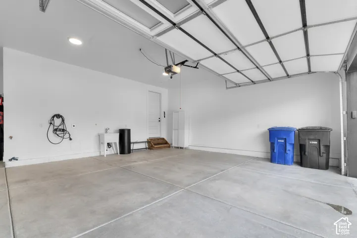 Multi-car garage featuring a concrete floor, recessed lighting, white-painted walls, an integrated utility sink, and an automated overhead door