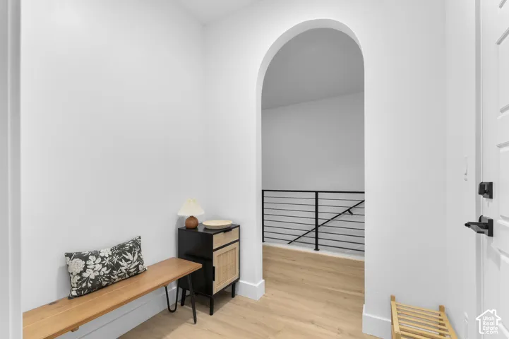 Arched entryway featuring neutral wall tones, wood-finish flooring, and a modern black metal horizontal-bar railing