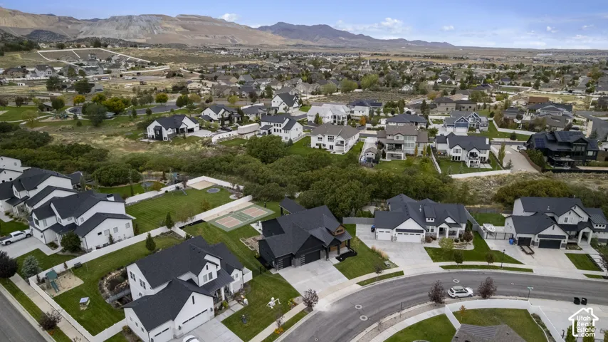Aerial perspective of a suburban neighborhood featuring paved cul-de-sac streets, manicured lawns, varied residential rooflines, and a backdrop of mountain ranges