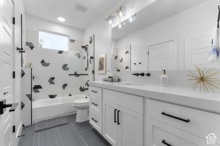 Bathroom featuring a white vanity with quartz countertop, wall-mounted matte black faucet, full-width mirror, and shower surround with geometric tile accents
