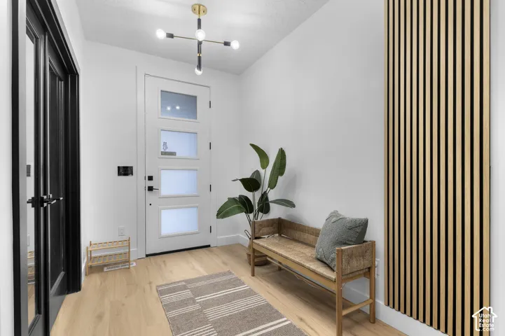Entryway featuring a wood-finish floor, white entry door with frosted glass panels, linear wood-slat wall paneling, and a contemporary multi-arm sputnik chandelier