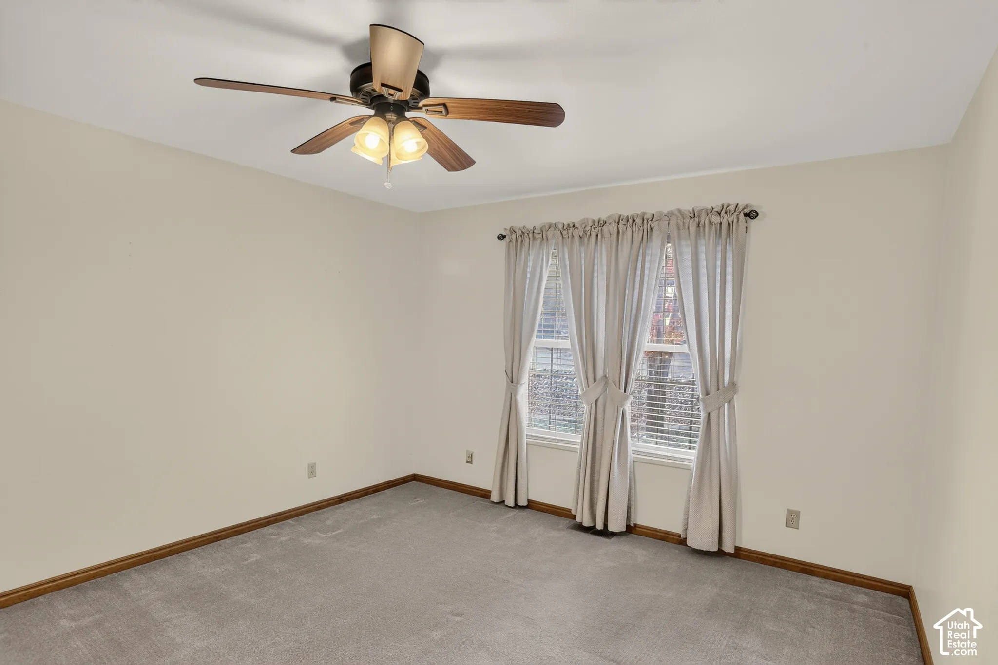Neutral-toned wall interior featuring carpeting, a multi-blade ceiling fan with integrated light fixture, and two windows