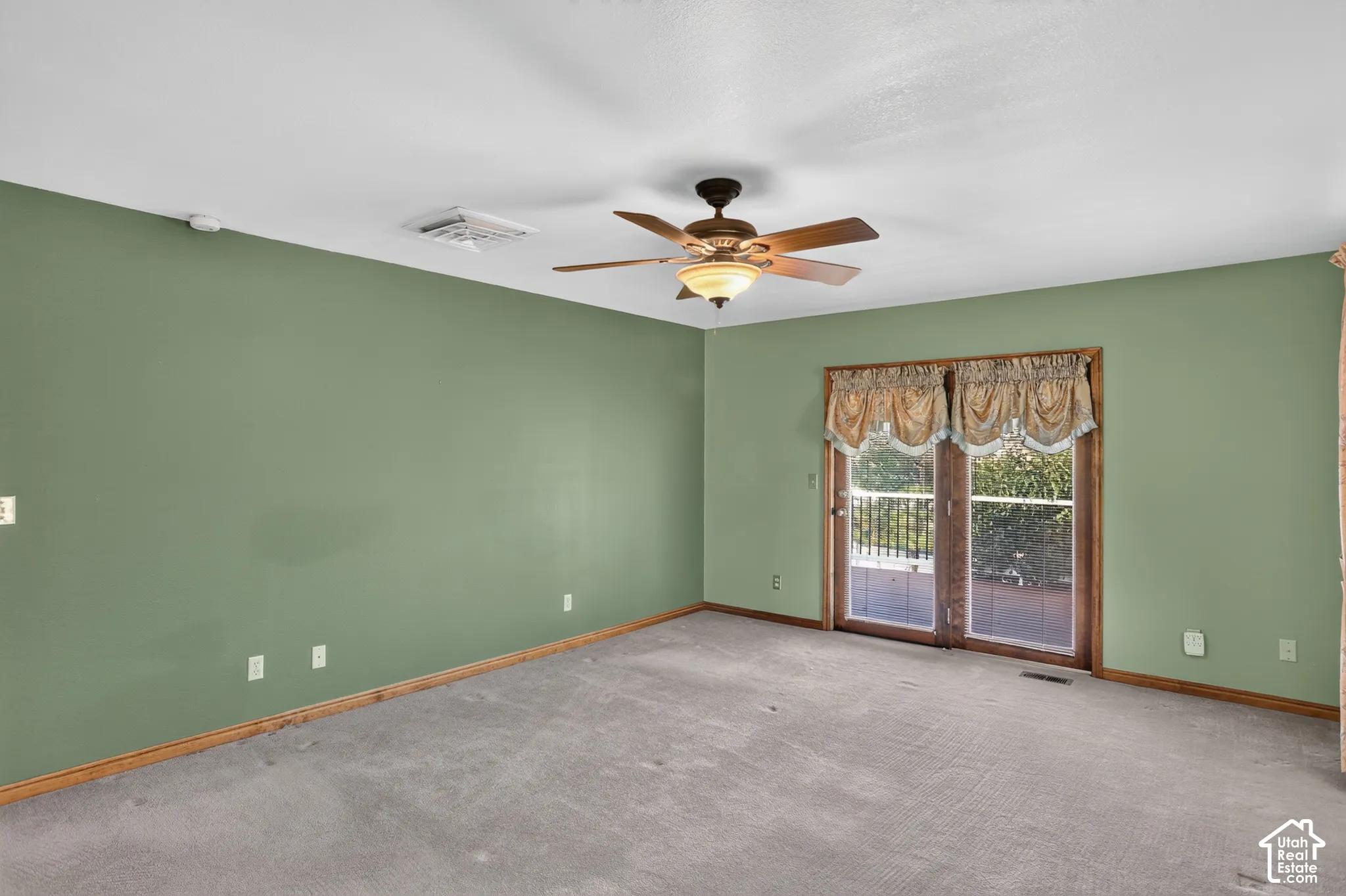 Room interior featuring neutral carpeting, a ceiling-mounted light fixture with a fan, and sliding glass doors with wood trim