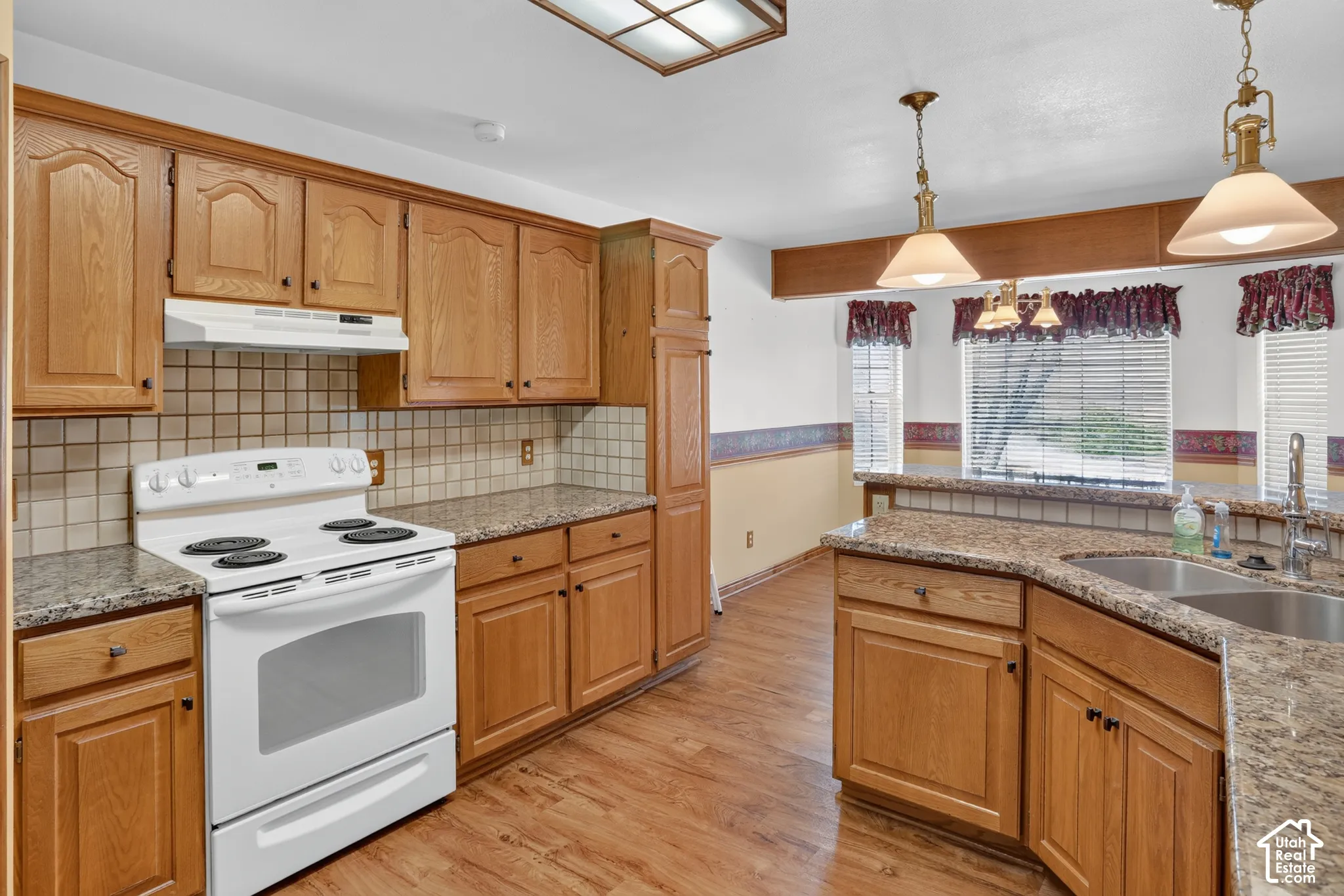 Kitchen featuring natural wood cabinetry, stone-surface countertops, square tile backsplash, wood-finish flooring, and pendant lighting