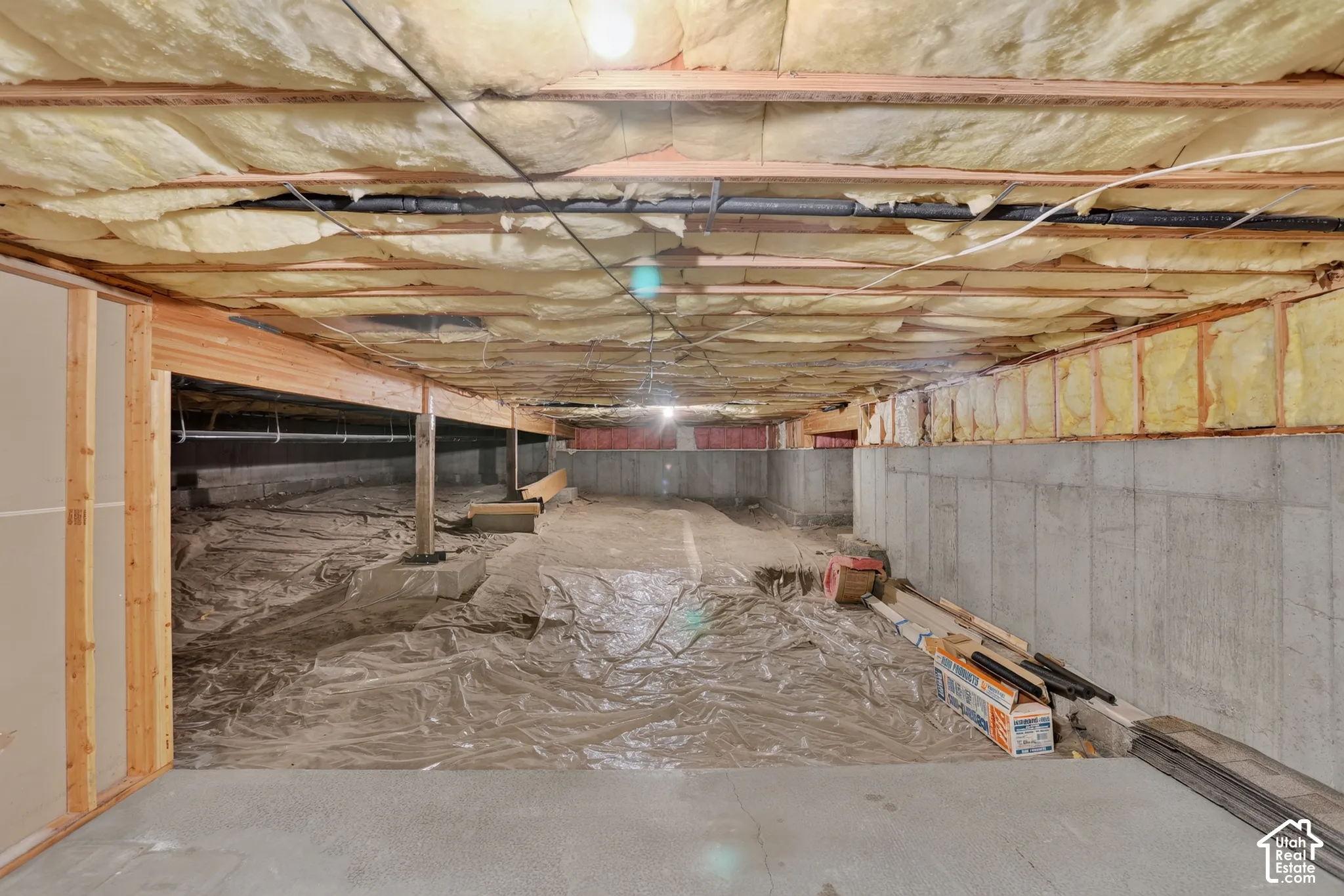 Unfinished lower level featuring concrete foundation walls, exposed timber framing, fiberglass batt insulation, and a vapor barrier floor covering