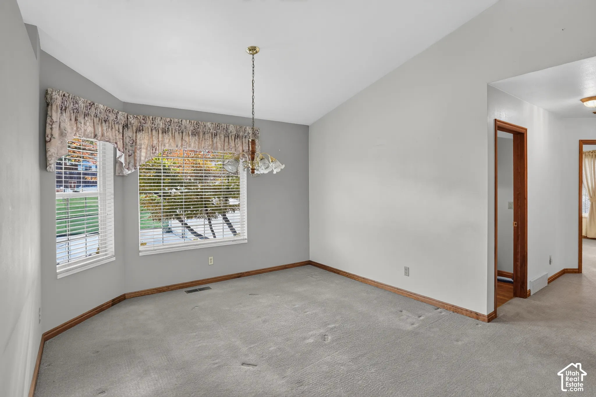 Vaulted ceiling, expansive bay window, and a decorative multi-light chandelier