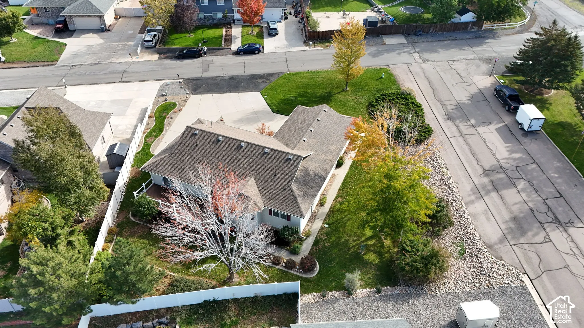 Aerial perspective featuring a multi-gabled roofline, concrete driveway, fenced yard, and mature landscaping
