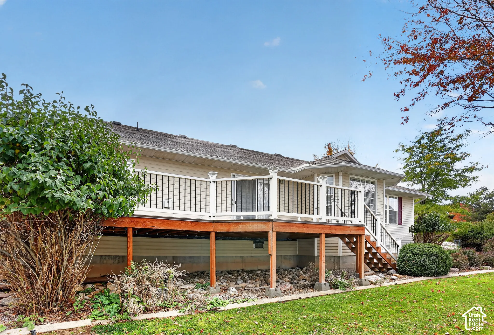 Raised wood deck featuring white railings, black metal balusters, and stairs, accented by exterior siding and a rock-landscaped yard