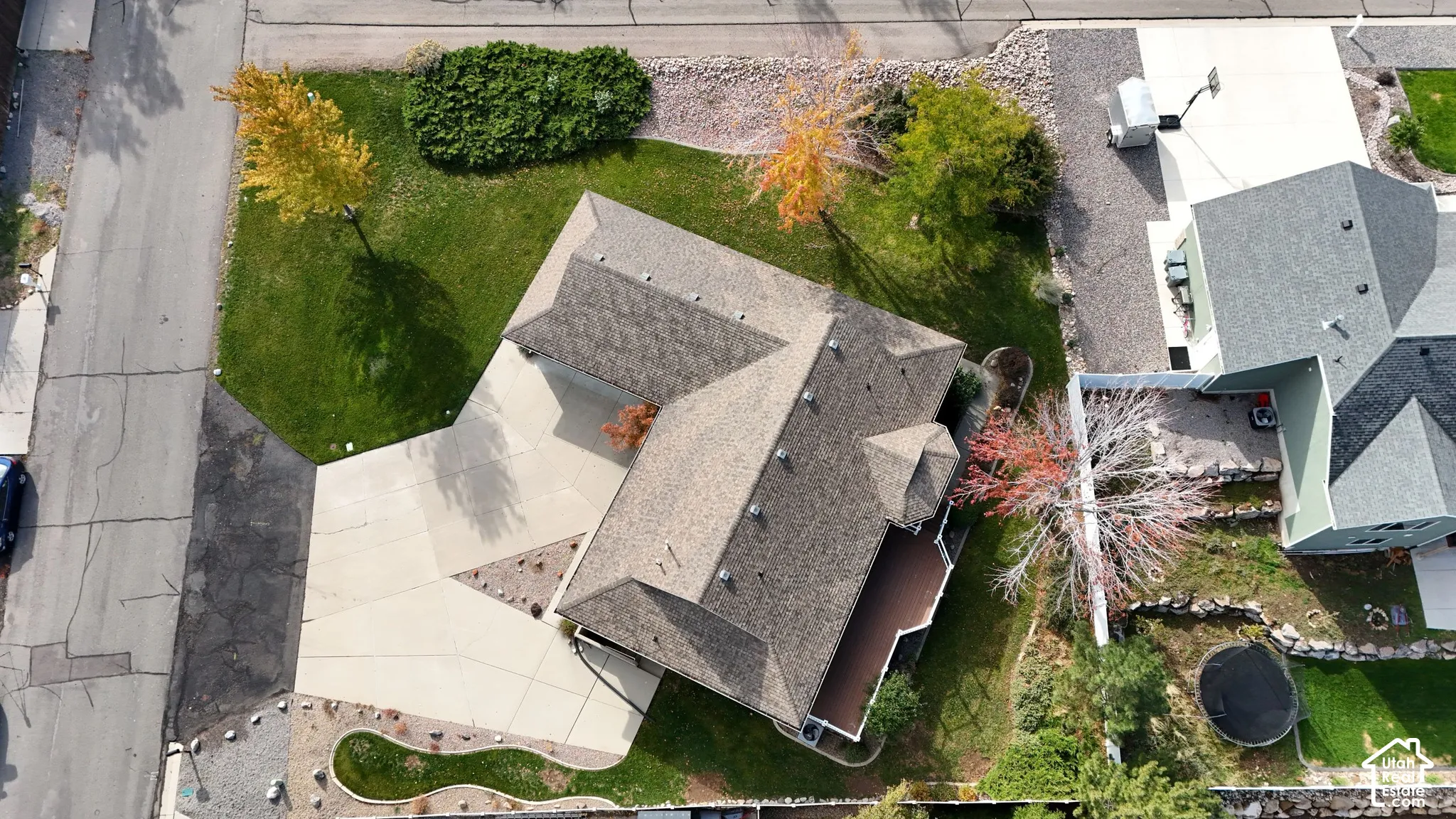 Aerial perspective of a multi-gabled roofline, concrete driveway, manicured lawn, and mature trees on a corner lot