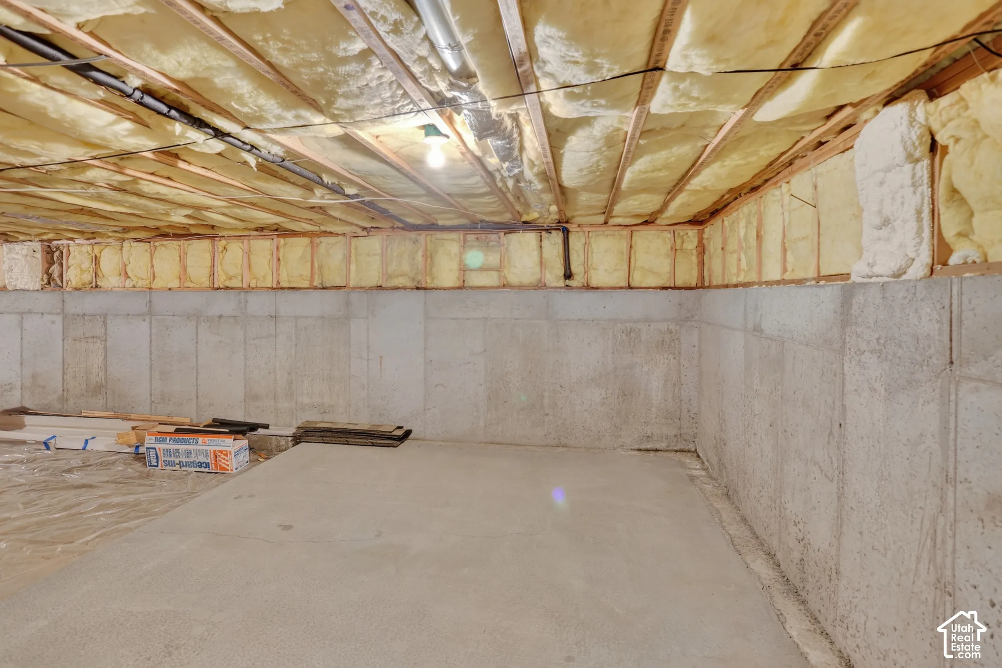 Unfinished storage area with poured concrete foundation walls, concrete floor, and exposed ceiling joists featuring spray foam insulation