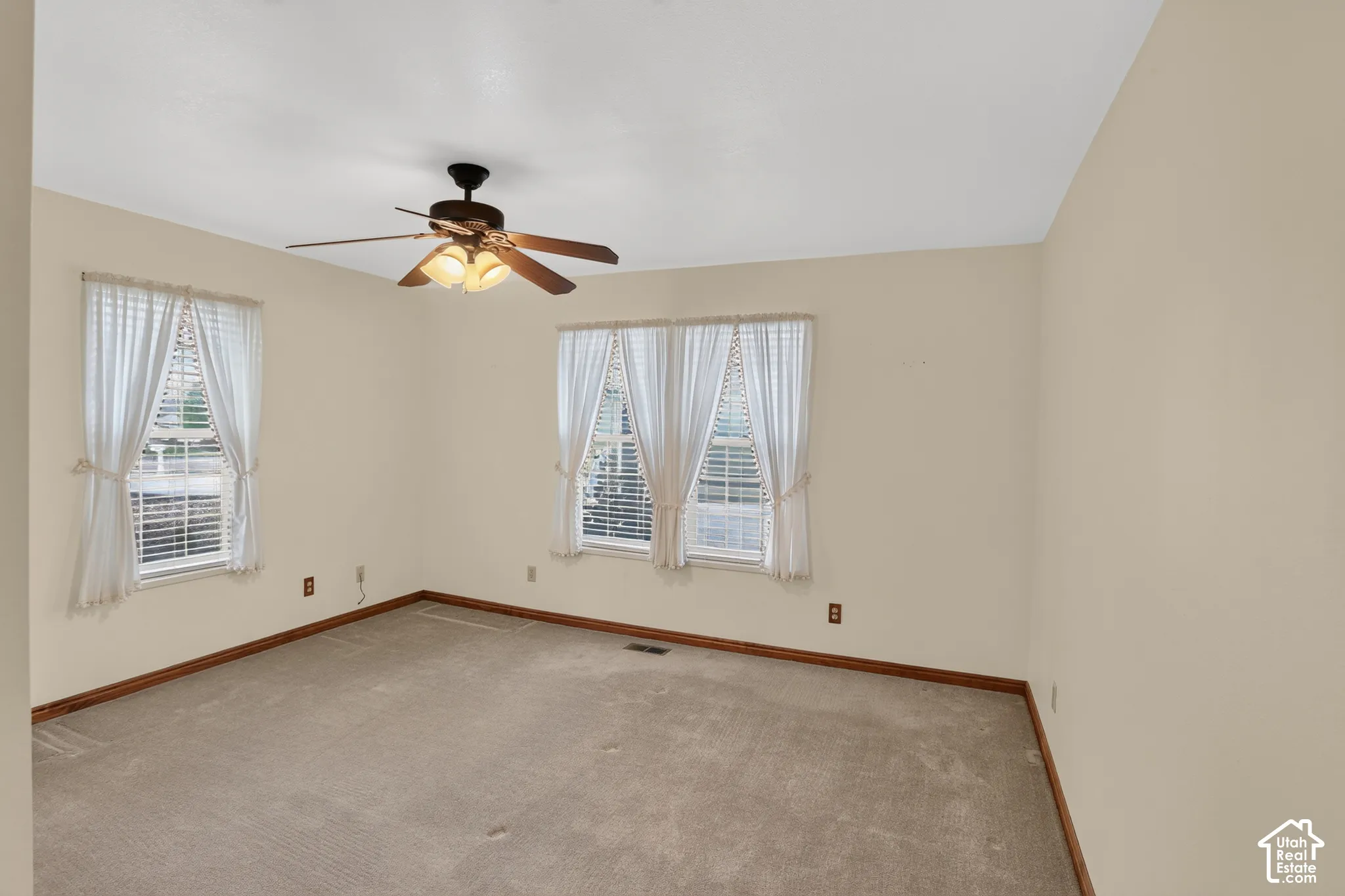 Neutral-toned interior space featuring wall-to-wall carpeting, wood-trim finishing, and a multi-blade ceiling fan with an integrated light fixture