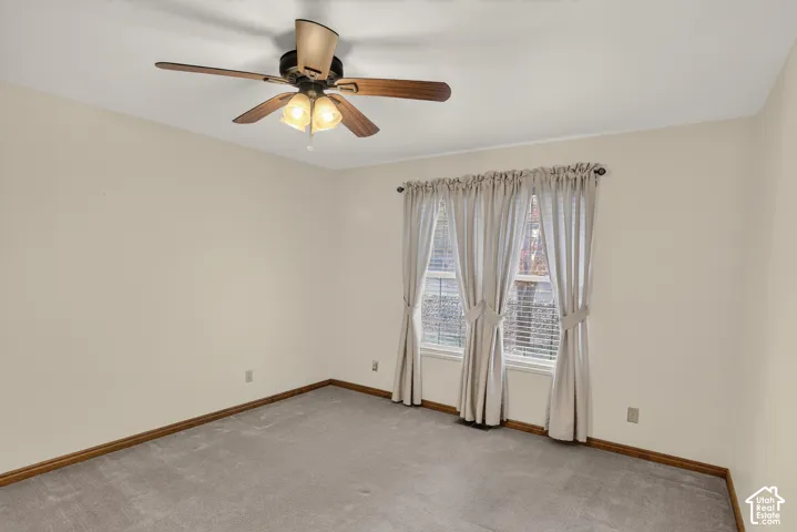 Neutral-toned wall interior featuring carpeting, a multi-blade ceiling fan with integrated light fixture, and two windows