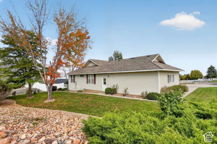 Exterior featuring light-colored horizontal siding, asphalt shingle roofing, mature landscape trees, and rock-mulched ground cover