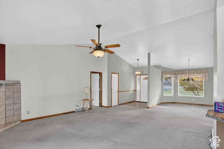 Vaulted ceilings, tiled fireplace surround, ceiling fan with light fixture, natural light from bay window, and pendant lighting