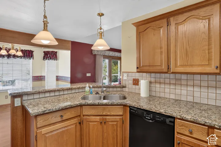 Kitchen featuring natural wood cabinetry, stone-finish countertops, dual-basin stainless steel sink, tile backsplash, and dual pendant lighting