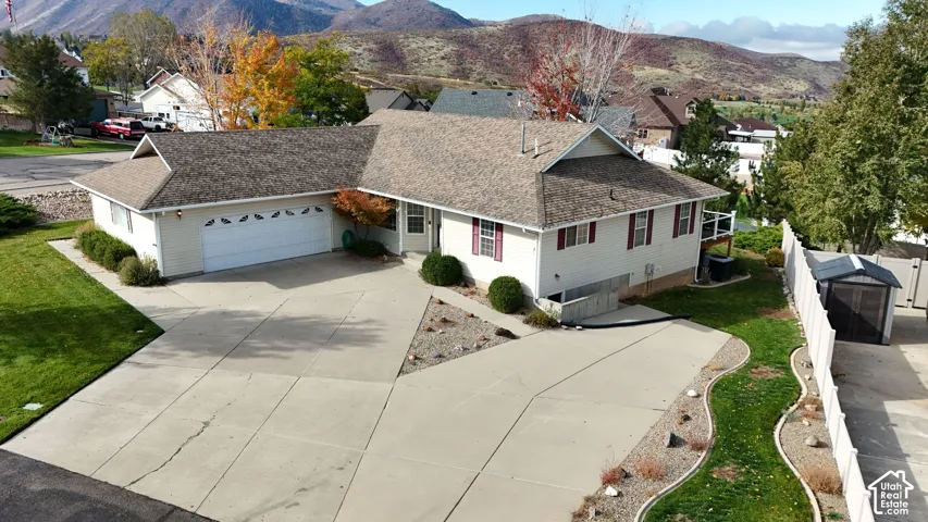 Single-story residence featuring light-colored siding, a multi-car garage, expansive concrete driveway, and a fenced yard with mountain backdrop