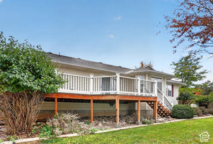 Raised wood deck featuring white railings, black metal balusters, and stairs, accented by exterior siding and a rock-landscaped yard