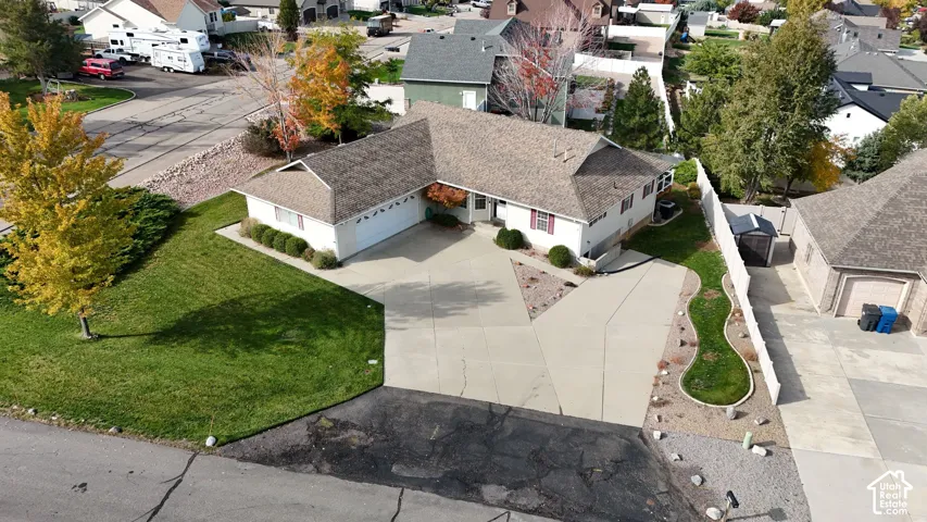 Single-story residence featuring a multi-car garage, expansive concrete driveway, asphalt shingle roofing, and landscaped yard with decorative edging