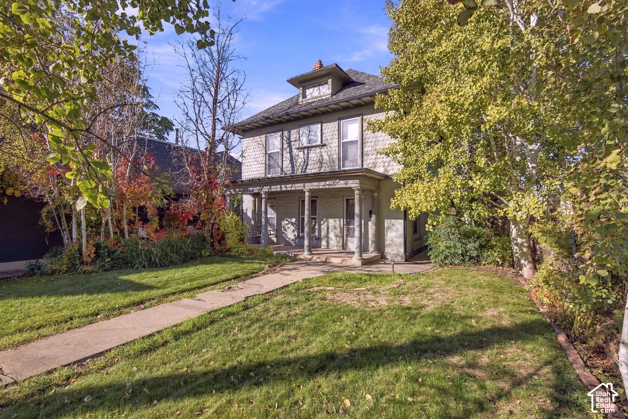 Two-story residence featuring shingle-style siding, a covered front porch with classical columns, a hipped roof with a dormer, and mature landscaping