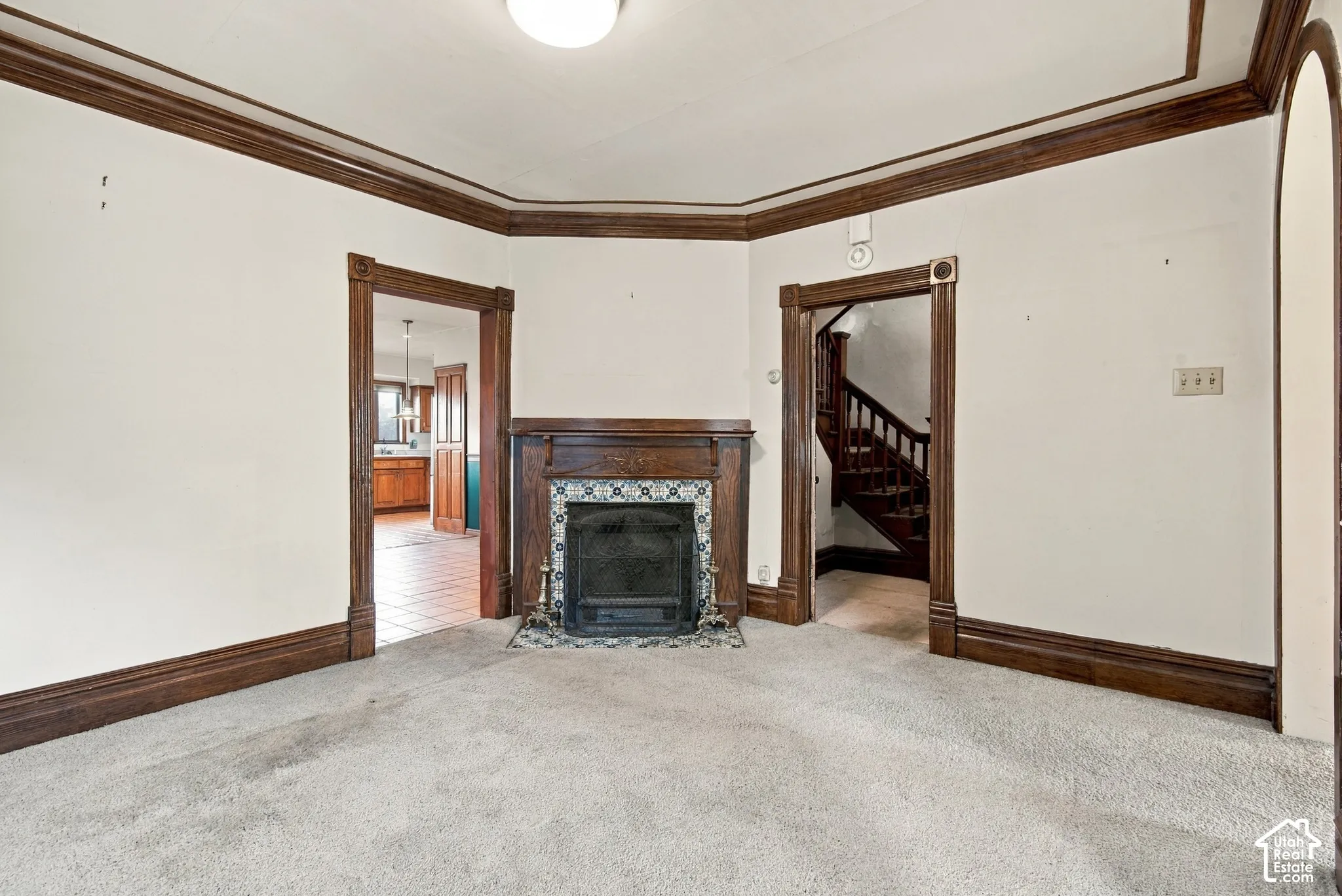 Interior featuring a wood-burning fireplace with decorative tile surround, dark wood crown molding, arched doorways, and original wood trim