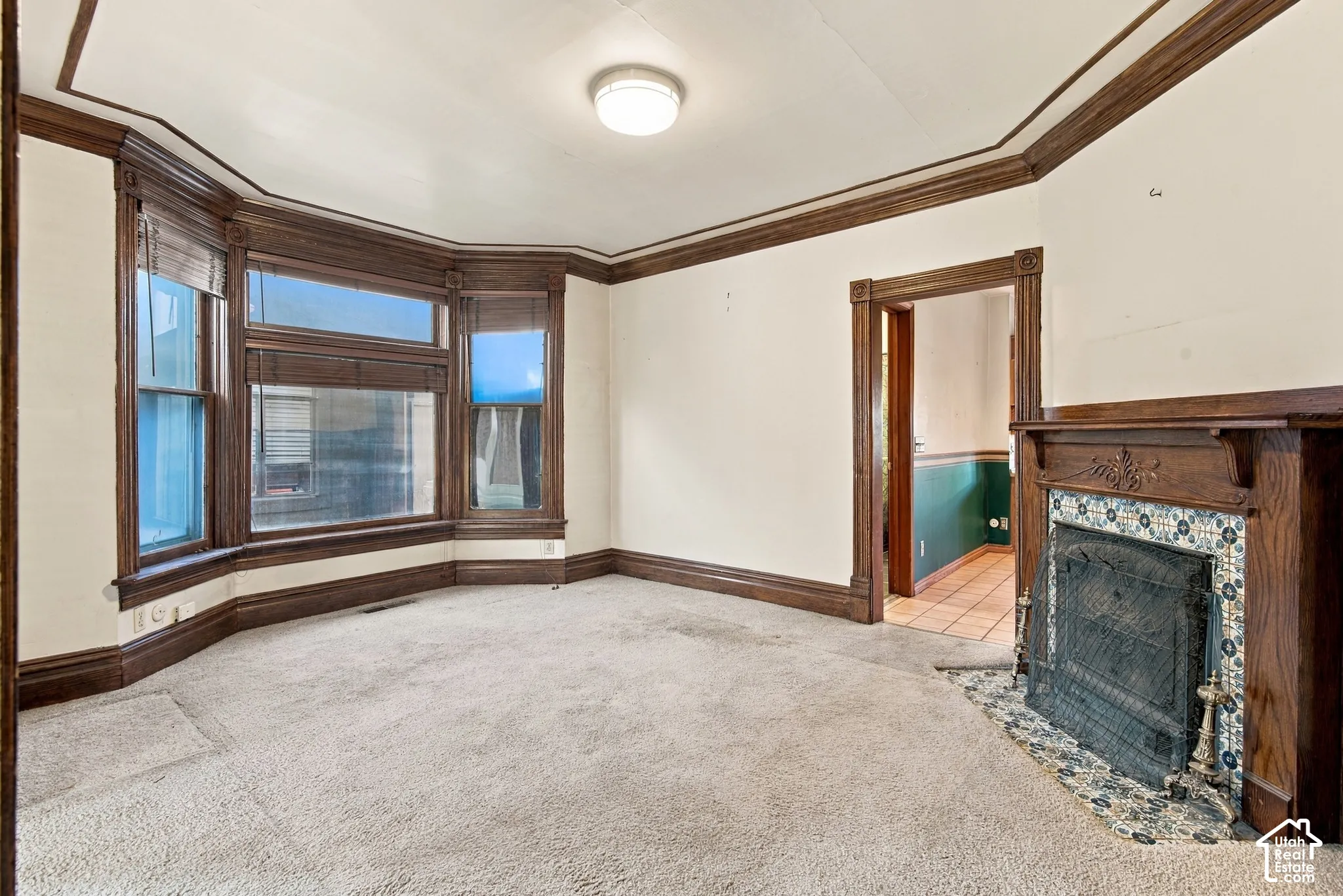 Bay window with wood trim, decorative fireplace featuring tile surround and wood mantel, crown molding, and wooden door casing