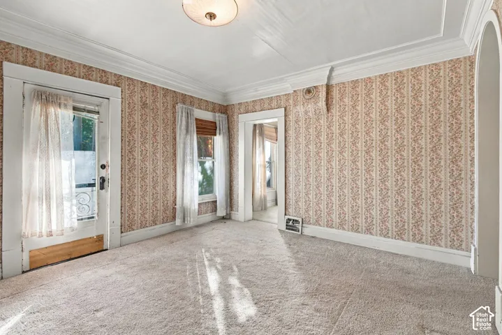 Interior space featuring ornate crown molding, patterned wallpaper, a central flush-mount ceiling light fixture, and arched doorway trim