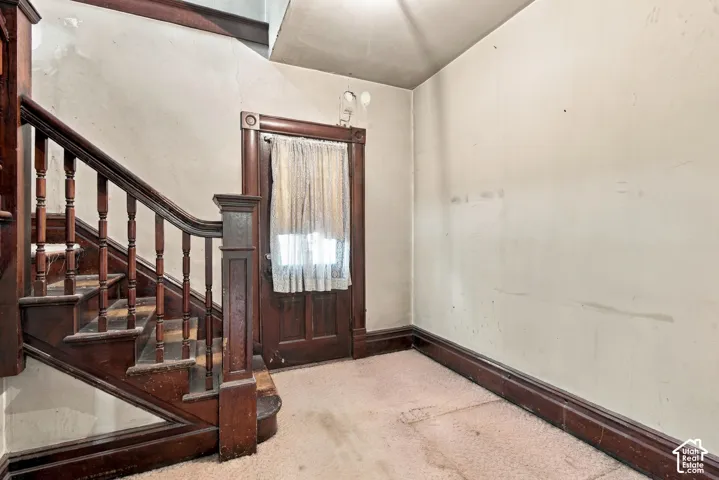 Staircase featuring dark-stained wood balusters and a prominent newel post, complemented by a solid wood entry door with ornate trim