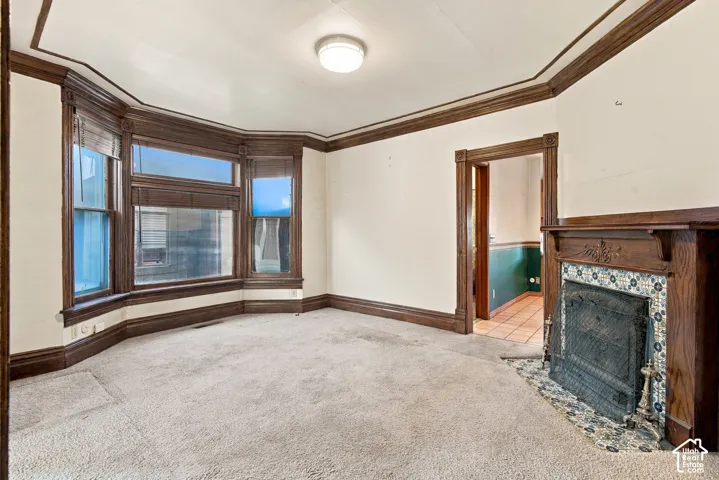 Bay window with wood trim, decorative fireplace featuring tile surround and wood mantel, crown molding, and wooden door casing