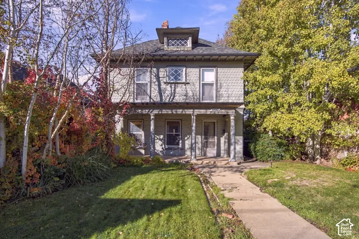 Two-story exterior featuring shingle-style siding, a covered front porch with classical columns, a hipped roof with a dormer, and patterned window detailing
