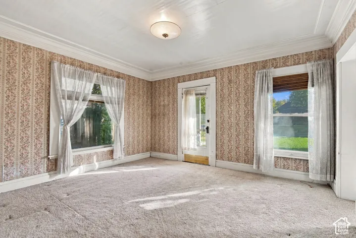Living space featuring crown molding, patterned wall coverings, high ceilings, carpeted flooring, and a glass-paneled exterior door