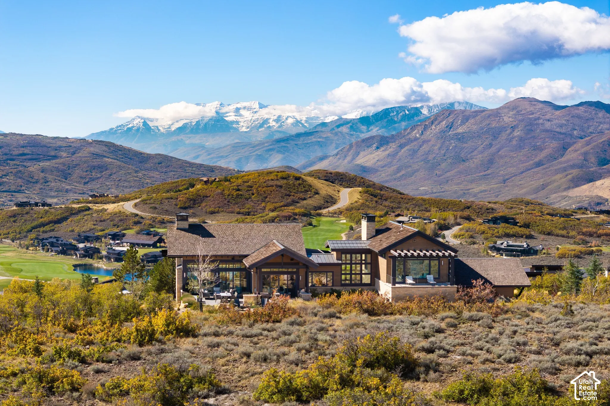 Custom residence featuring a multi-gabled roofline, stone and timber exterior, expansive floor-to-ceiling windows, and a paved outdoor patio, all set against a mountainous backdrop
