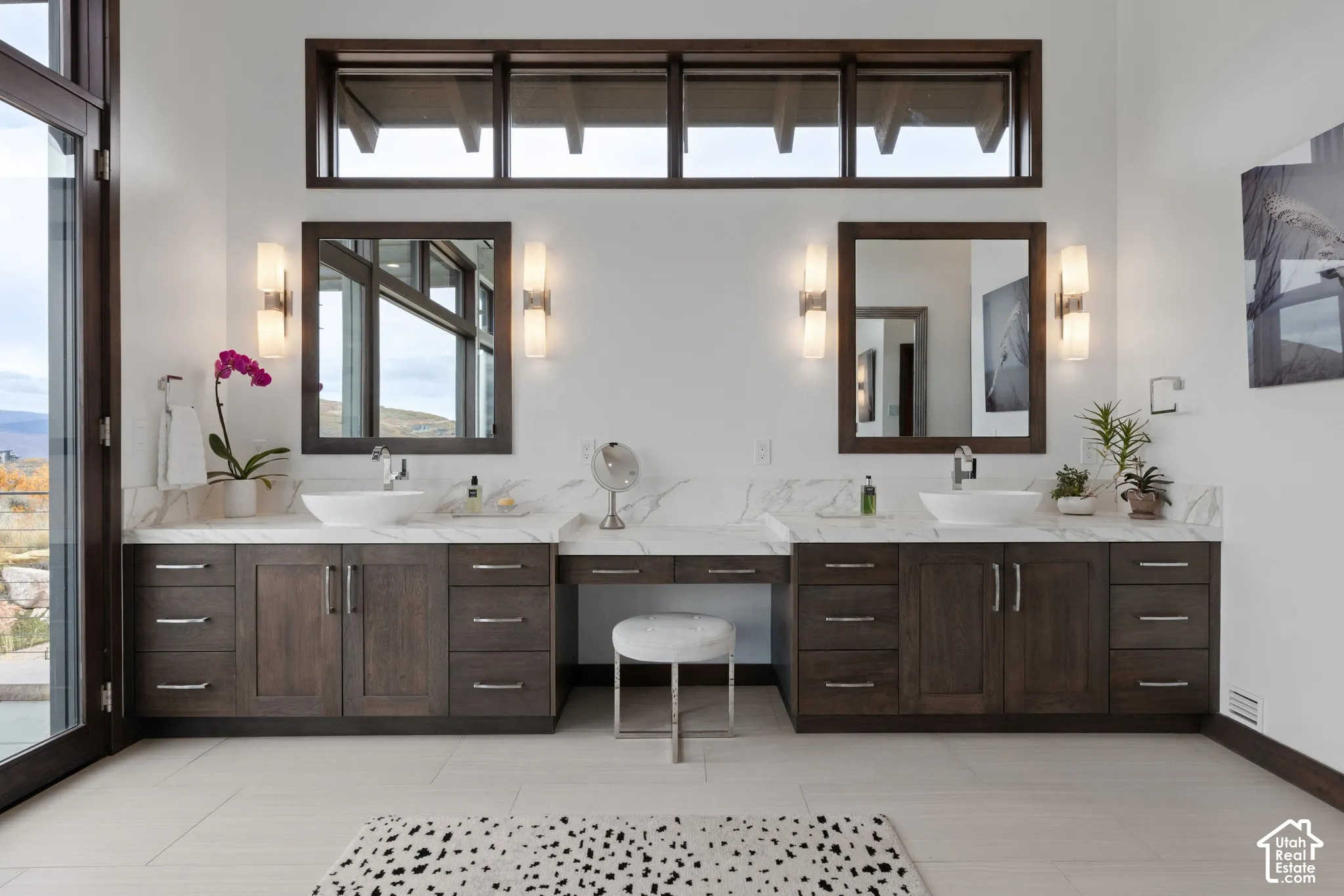 Dual-vanity cabinetry with integrated makeup station, stone-finish countertops, vessel sinks, rectangular wall-mounted mirrors, and transom windows