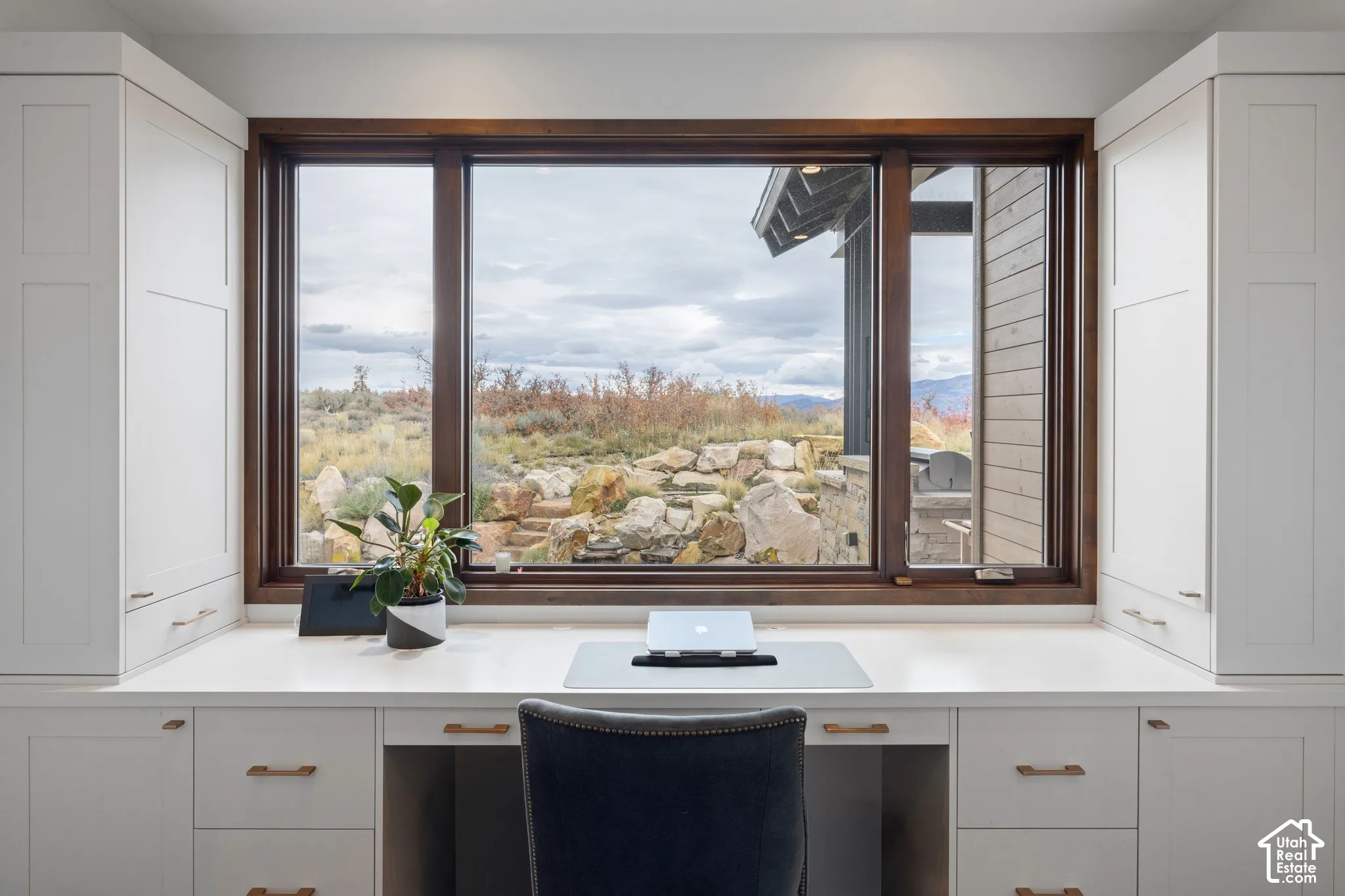 Built-in white cabinetry with shaker-style doors, expansive picture window with dark wood trim, stone-topped desk, and metal hardware