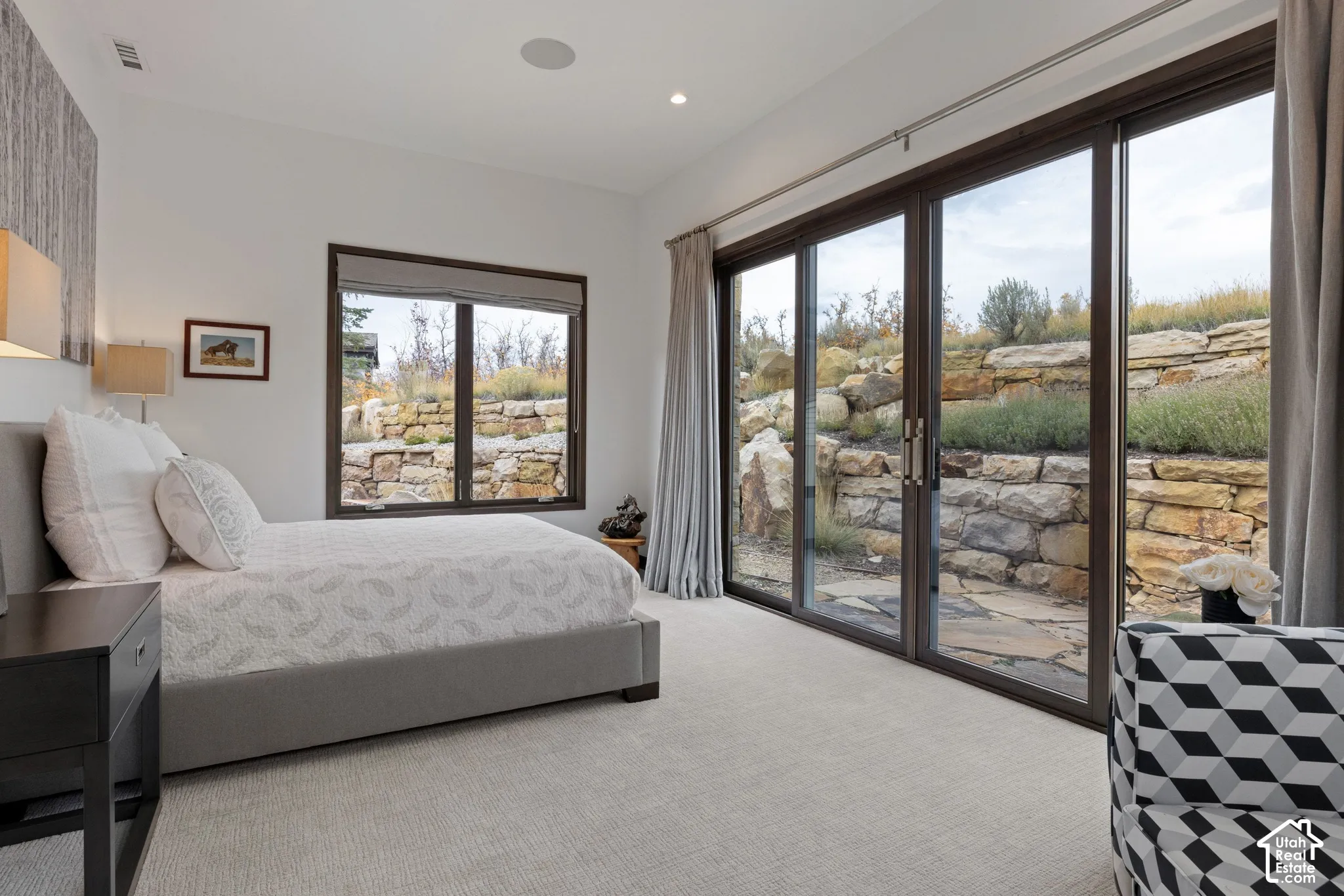 Multi-panel sliding glass doors, carpeted flooring, neutral wall finish, and a natural stone retaining wall