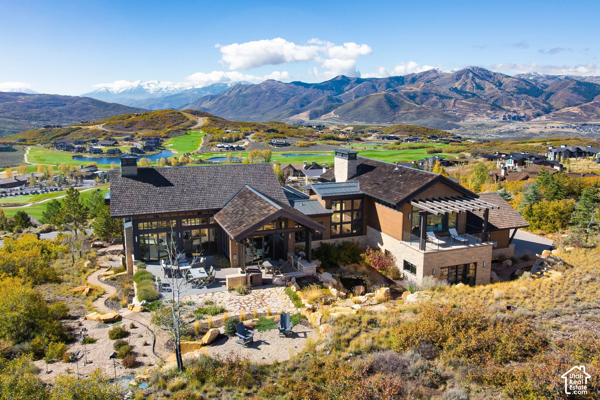 Mountain estate featuring a shingle roof, stone and wood exterior siding, a multi-level flagstone patio, and a pergola-covered deck