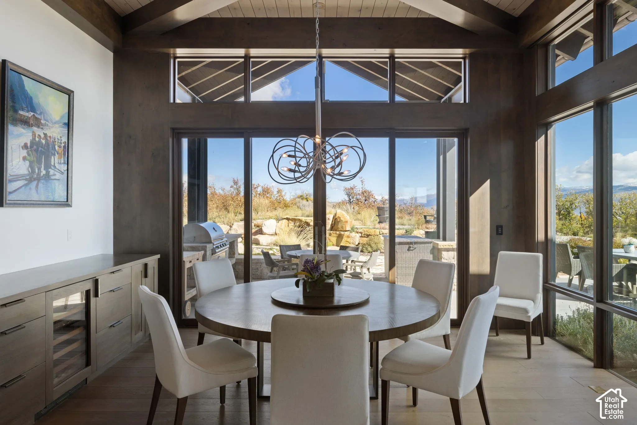 Vaulted ceiling with exposed wood beams, floor-to-ceiling windows, custom built-in cabinetry with integrated wine cooler, and expansive glass sliding doors