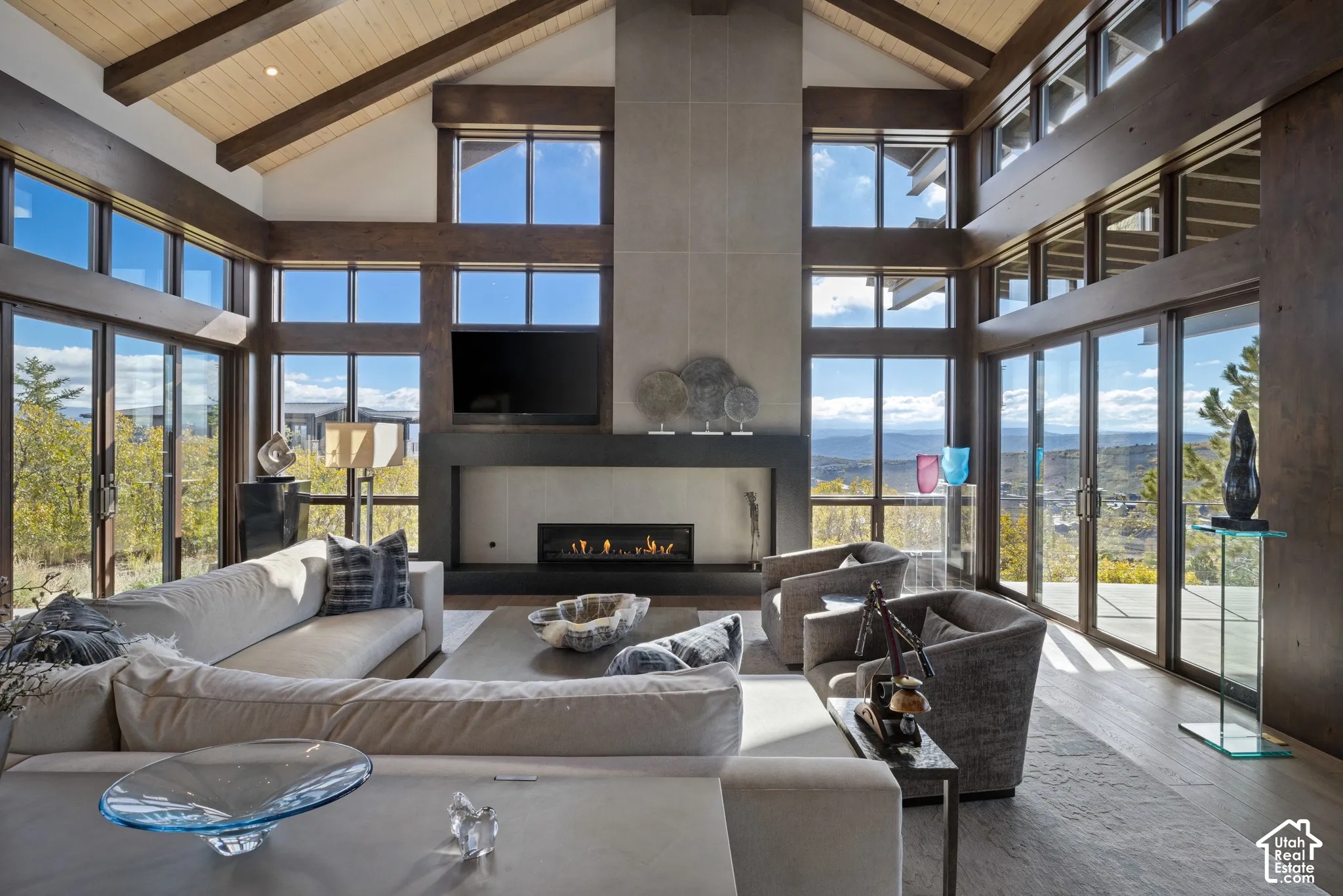 Vaulted ceiling with exposed wood beams, floor-to-ceiling windows, full-height stone-finish fireplace surround, and linear gas fireplace