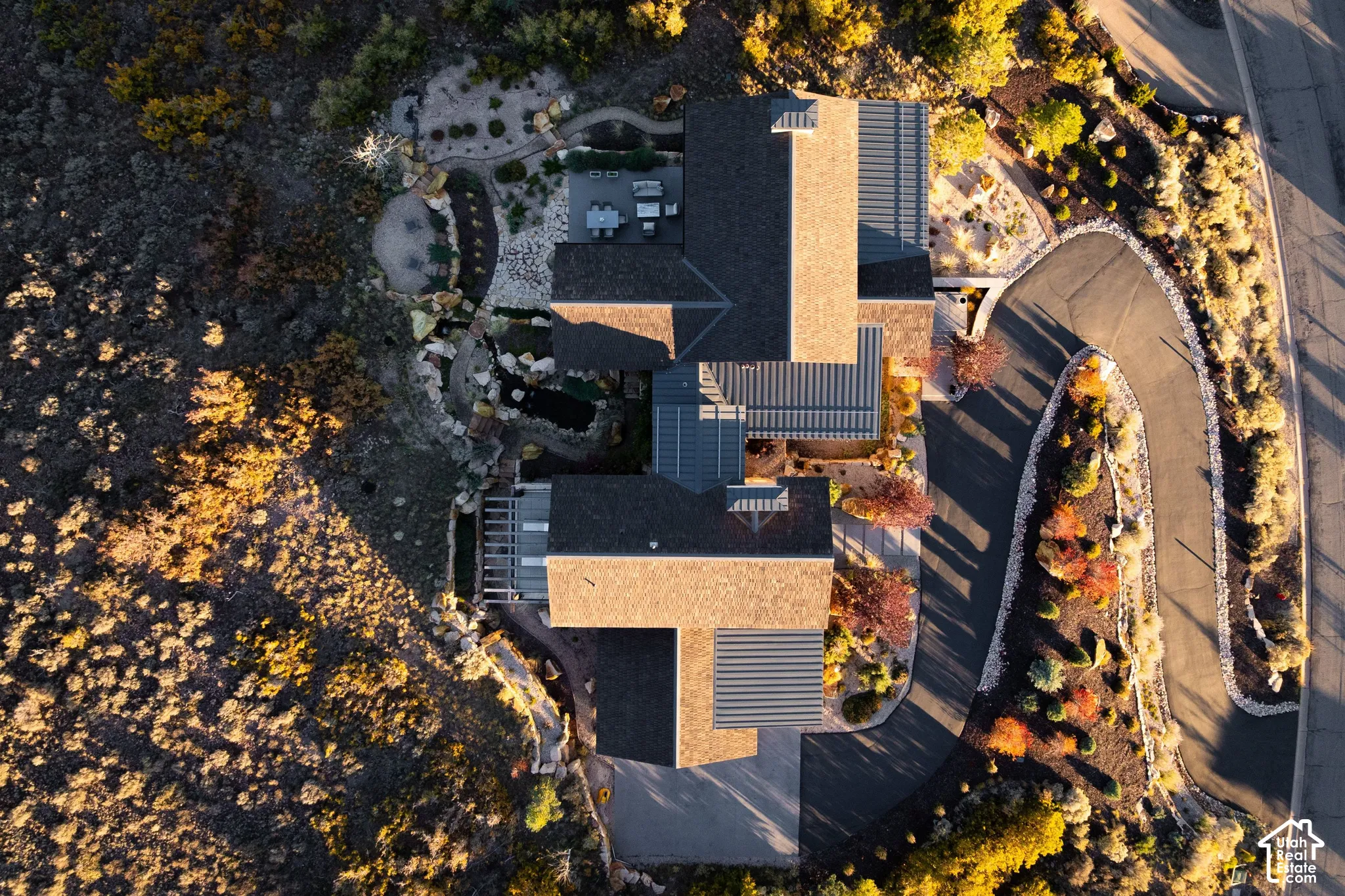 Aerial perspective of property featuring a multi-pitched roofline with solar panels, a paved driveway, natural stone hardscaping, and a water feature