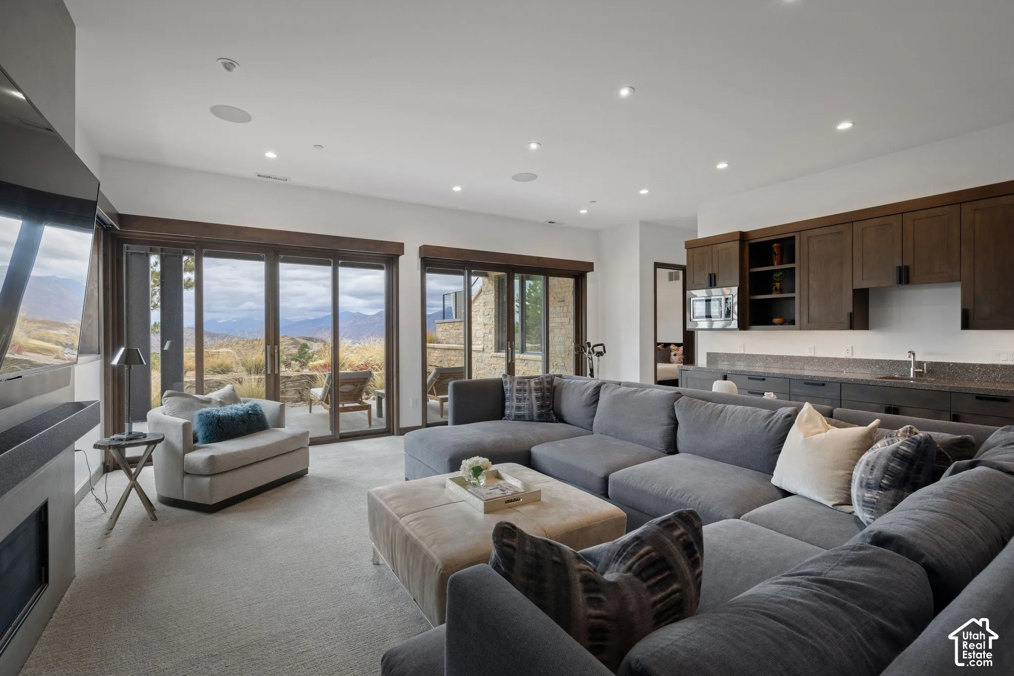 Living area featuring recessed lighting, a floor-to-ceiling stone fireplace, dual sliding glass doors, and built-in cabinetry with integrated sink and microwave