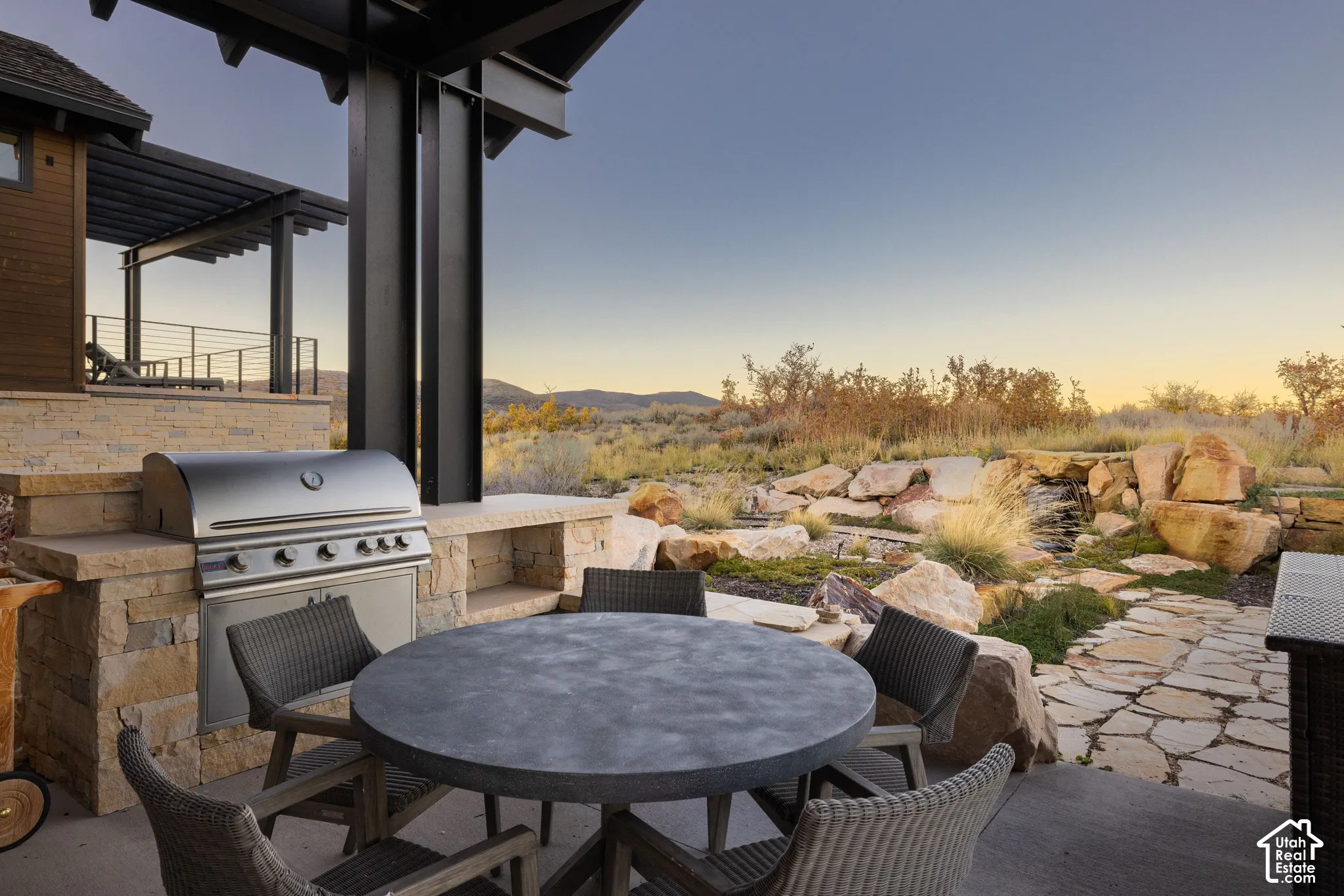 Covered outdoor kitchen featuring stone masonry, built-in stainless steel grill, natural stone hardscaping, and steel structural support beams