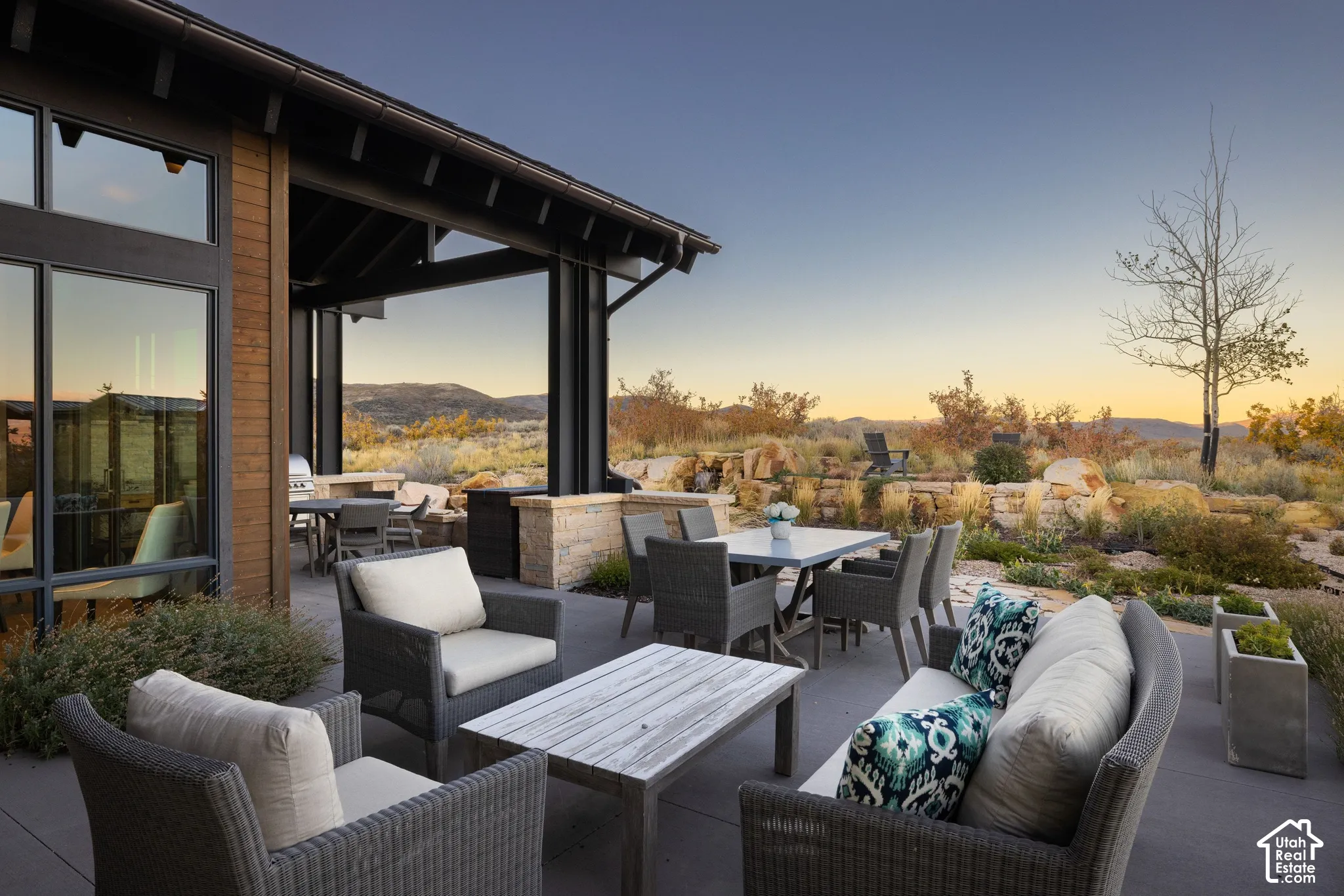 Covered patio featuring wood-toned siding, concrete flooring, stone masonry accents, and expansive glass window panels