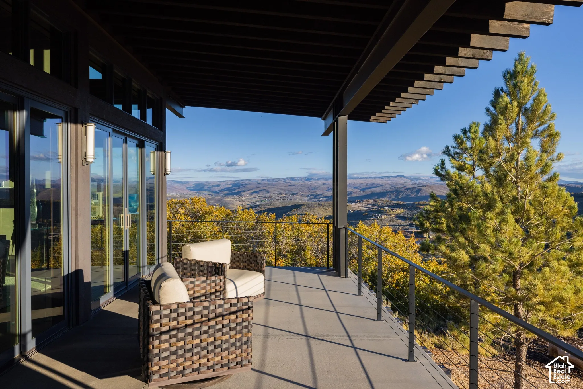 Covered patio featuring an exposed rafter ceiling, metal cable railing system, glass sliding doors, and expansive mountain scenery