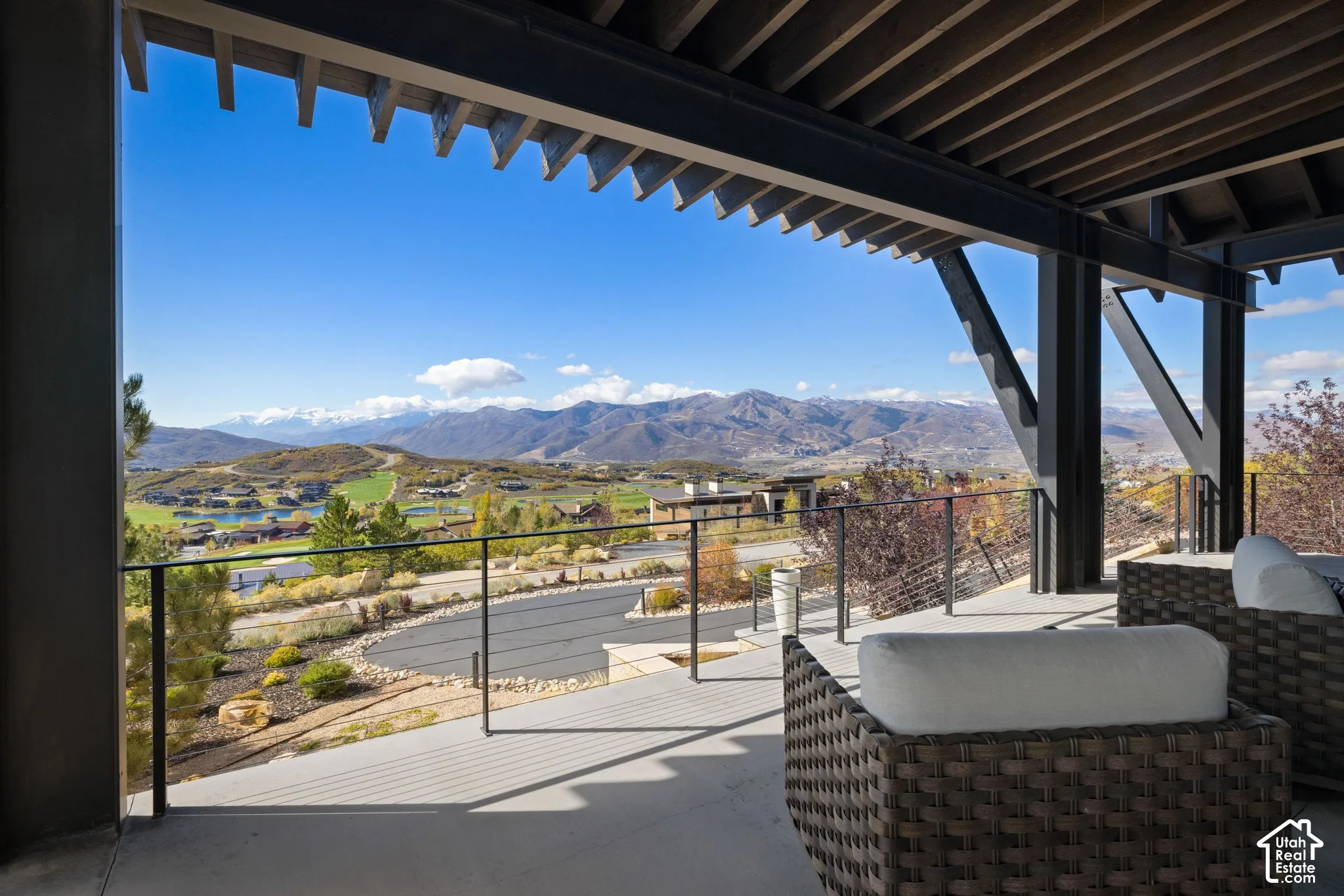 Covered patio featuring an exposed structural steel frame, open-slat ceiling, concrete flooring, and metal railing overlooking mountainous terrain