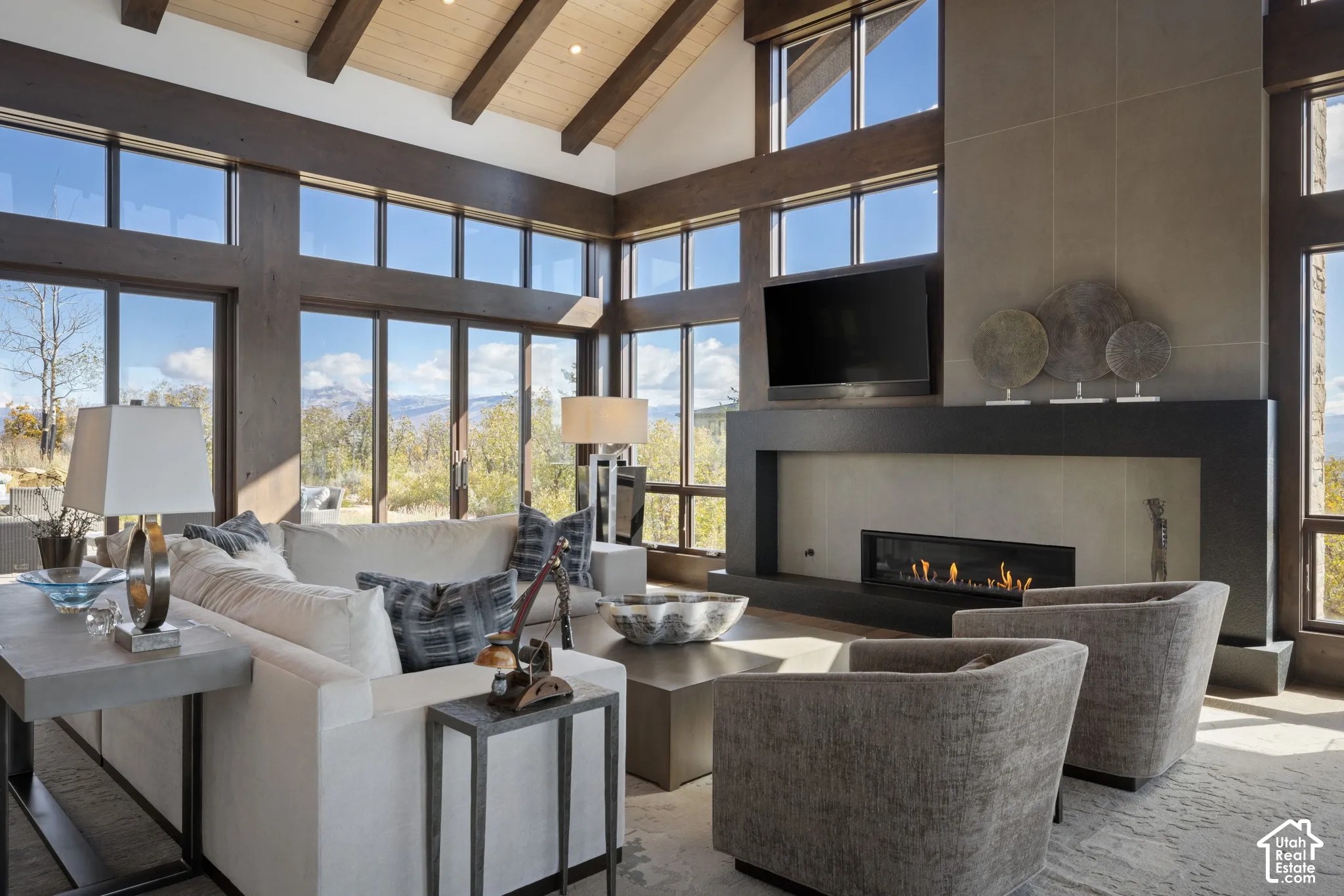 Vaulted ceiling with exposed wood beams, expansive floor-to-ceiling windows, and a full-height stone fireplace surround with a linear hearth