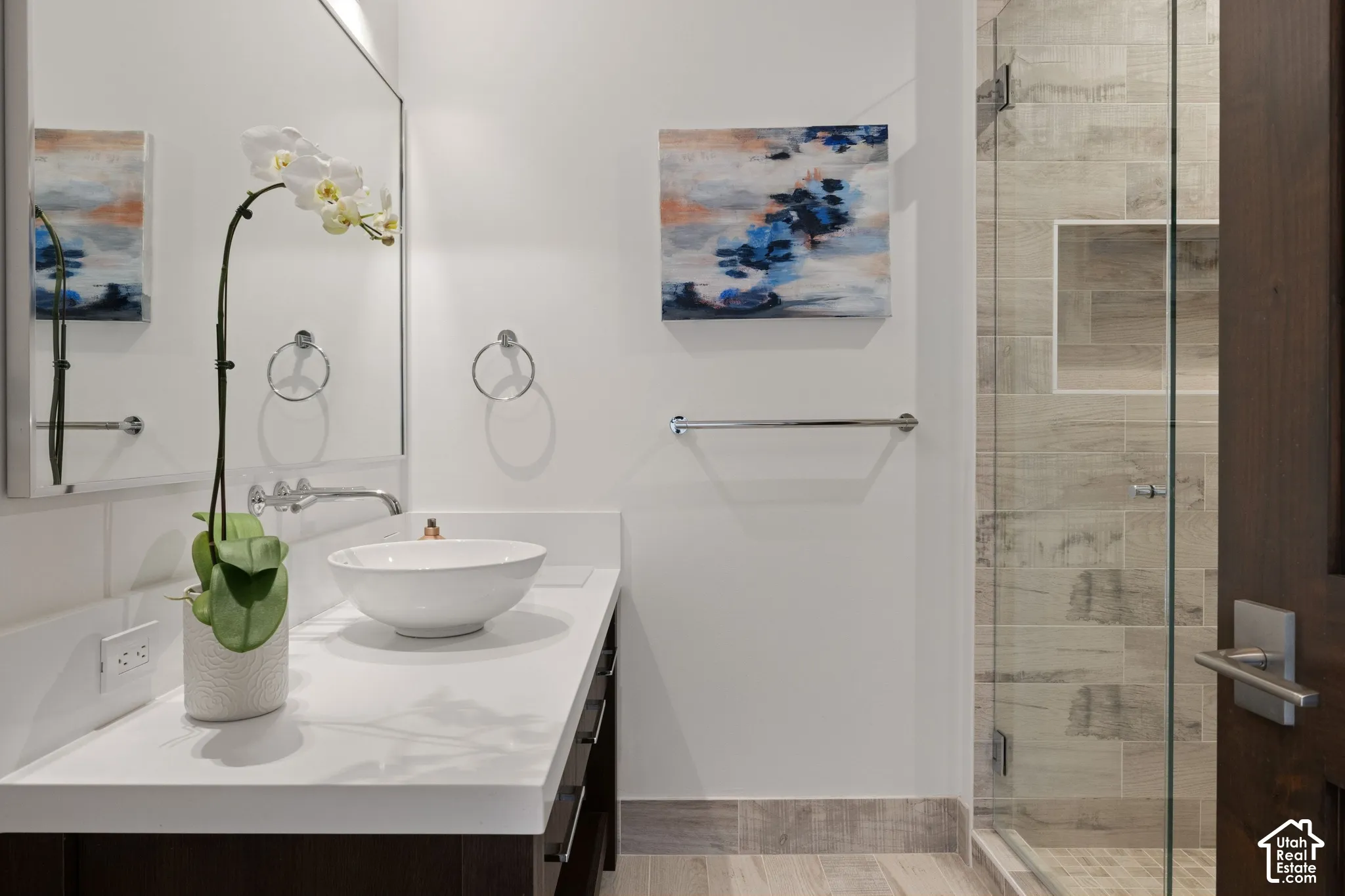 Vanity with solid surface countertop, white vessel sink, wall-mounted chrome faucet, large mirror, and glass-enclosed shower with built-in tile niche