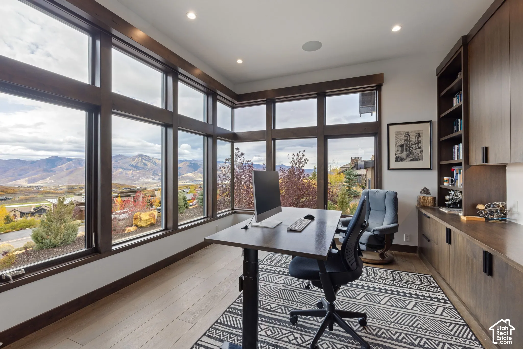 Expansive floor-to-ceiling windows with mountain scenery, custom built-in dark wood cabinetry, wood-finish flooring, and recessed ceiling lighting