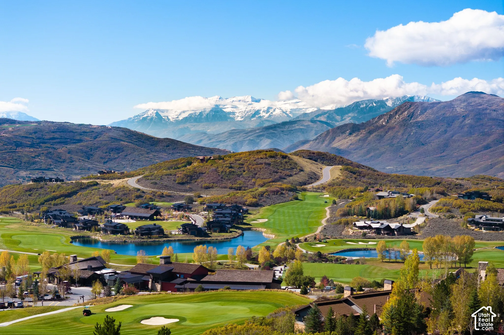 Aerial panorama featuring a golf course, multiple water features, and a backdrop of mountain ranges