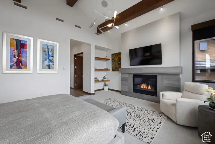 Vaulted ceiling featuring exposed dark wood beams, fireplace with large-format grey tile surround, built-in wooden shelving, and modern multi-arm pendant lighting