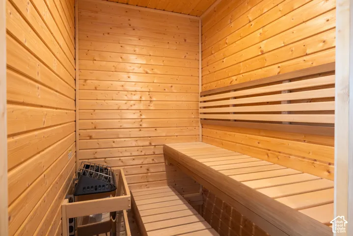 Sauna featuring natural wood tongue-and-groove wall paneling, built-in tiered wooden benches, and an integrated stone-filled electric heater with a protective wooden guard