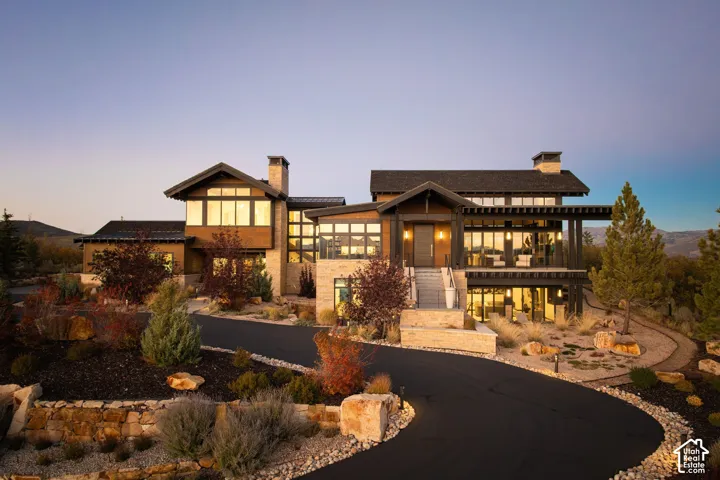 Architectural exterior featuring multi-level stone and wood-finish siding, extensive floor-to-ceiling windows, dual chimneys, and an expansive covered deck with exposed beam rafters